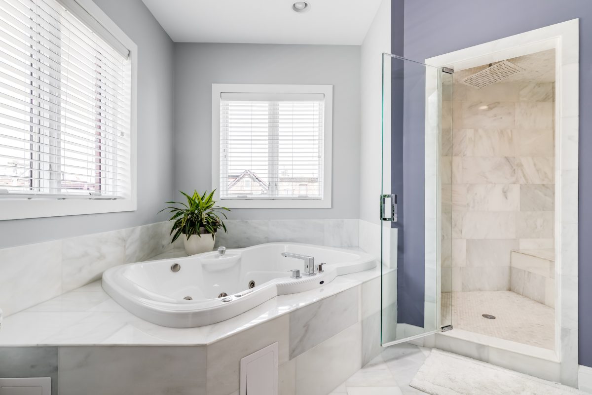 A large bathtub surrounded by marble tiles and a stand up tiled shower with a bench seat.