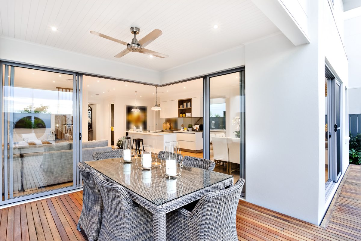 A stylish all- wicker dining table on the porch with wicker chairs and a wicker table with a glass top and stylish candles on the table top, separated from the house with glass sliding doors